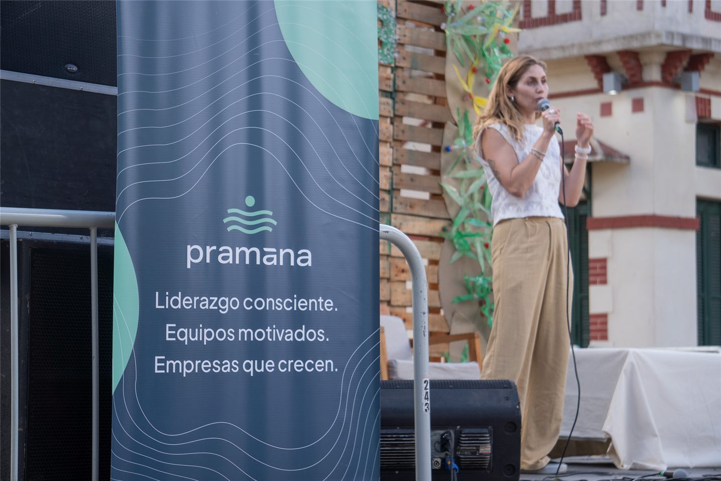 Facilitadora de Pramana con micrófono, junto a un banner de la marca